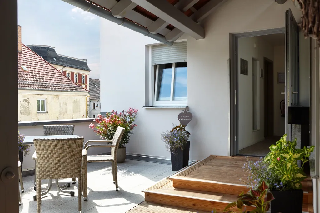 Dachterrasse mit Rattanmöbeln und Blumen vor einer Zimmertür