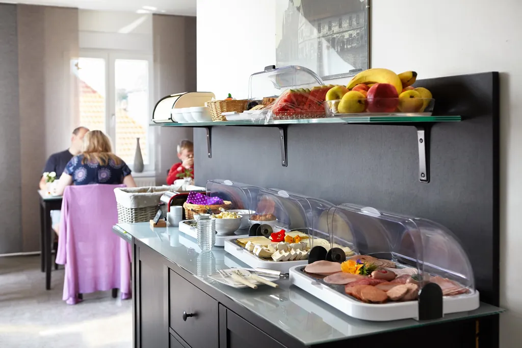 Frühstücksbuffet mit Aufschnitt, Obst und Brotkorb, Gäste am Tisch