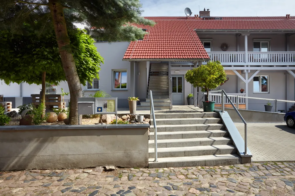 Das Haus der Pension Schlossgasse mit rotem Ziegeldach und Außentreppe, davor Kopfsteinpflaster