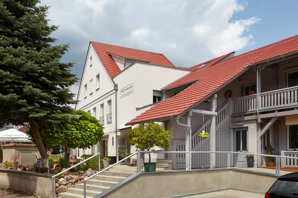 Pension mit rotem Ziegeldach, Balkon und großem Nadelbaum, Blick von der Treppe