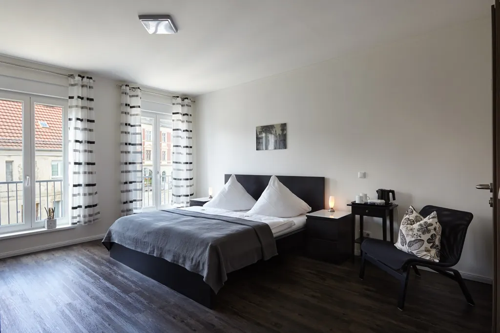 Helles Doppelzimmer mit Doppelbett, Sessel und bodentiefen Fenstern