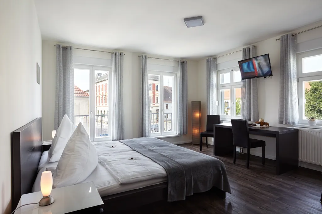 Zimmer mit Doppelbett, Fernseher und Schreibtisch vor großen Fenstern